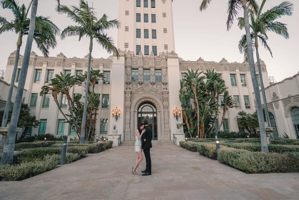 Couple standing beneath the grand archway of Beverly Hills City Hall during evening engagement photos