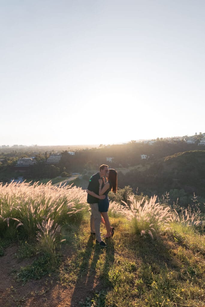 Couple kissing among golden fountain grass at sunset on a Beverly Hills hillside during an engagement photo session