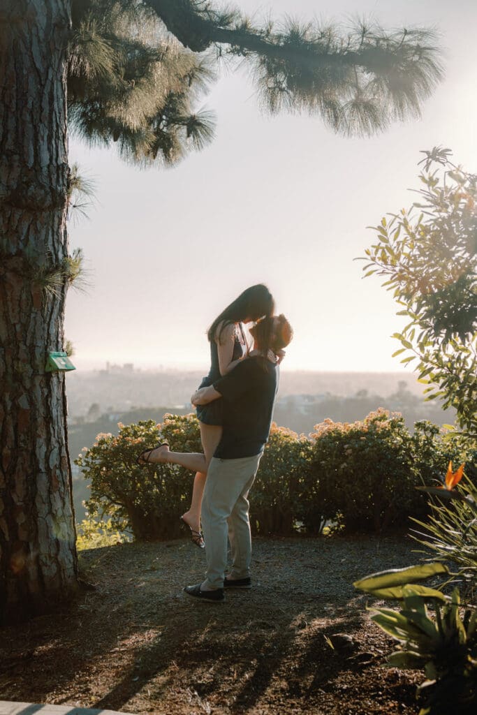 Couple embracing with a lift against the LA skyline during a Beverly Hills engagement session in the Trousdale Estates hills