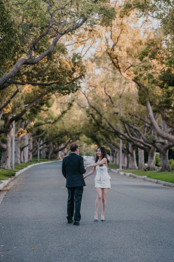 Groom spinning bride under a tree canopy on a Beverly Hills residential street during engagement photos