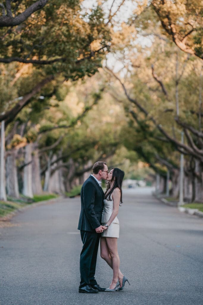 Couple embracing on a quiet tree-lined Beverly Hills street with soft afternoon light filtering through the canopy