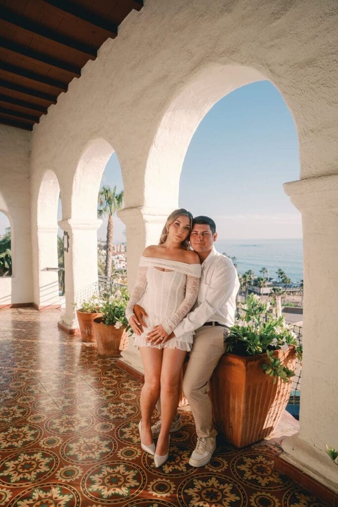 Couple posing in the arched walkway with ocean views during a Casa Romantica engagement session in San Clemente.