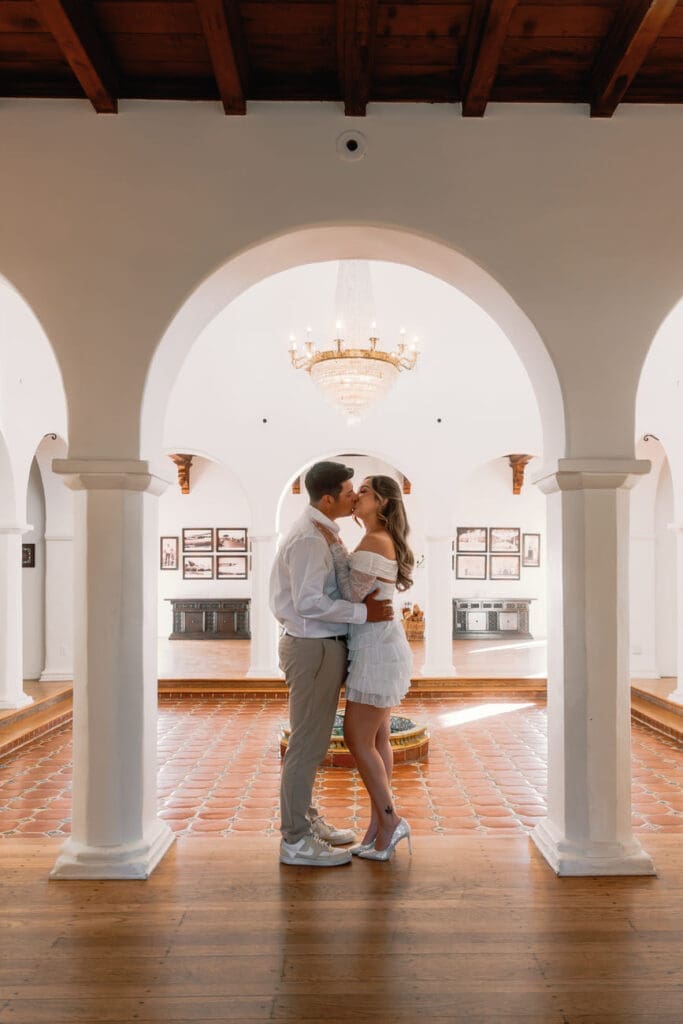 Couple embracing beneath the arches in the main salon at Casa Romantica during their engagement photos.