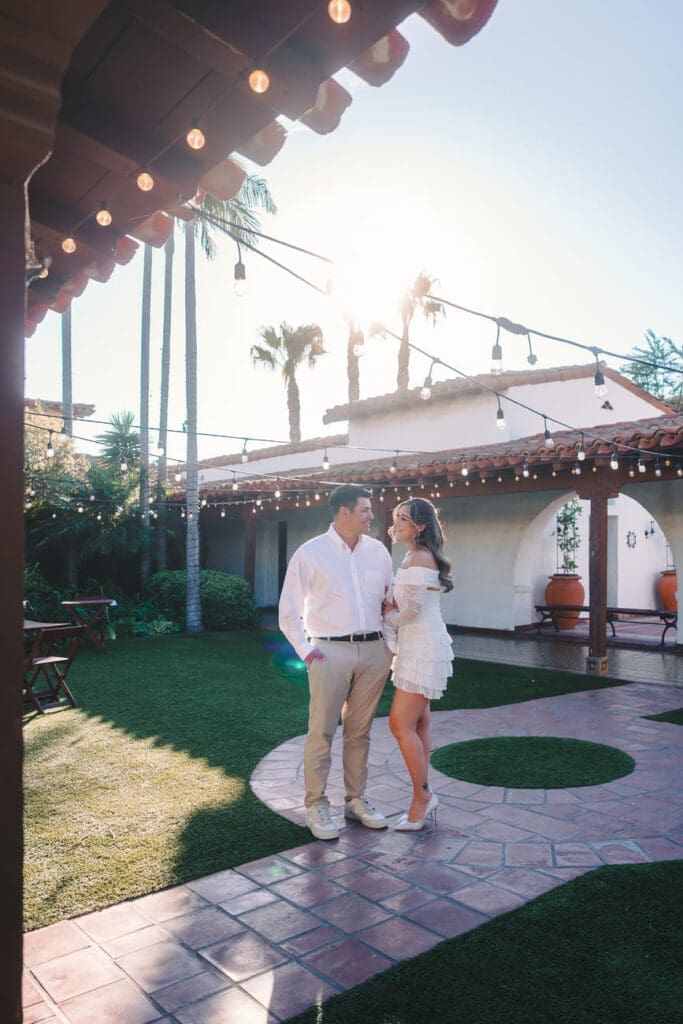 Couple standing beneath string lights in the ocean view courtyard at Casa Romantica in San Clemente, California.