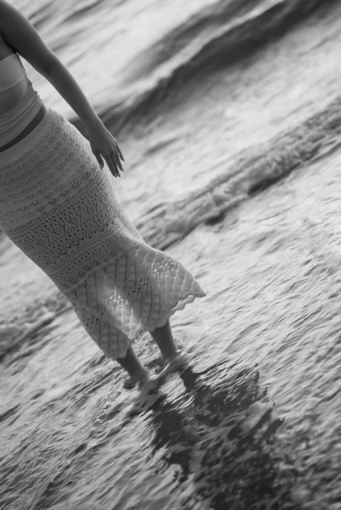 Black and white photo of a couple walking in the ocean during their San Clemente Beach engagement session.