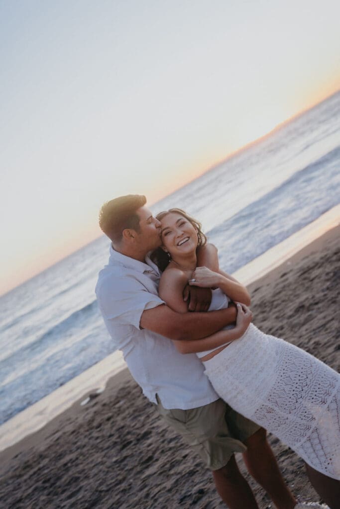 Couple laughing together on San Clemente Beach during coastal engagement photos in Orange County.
