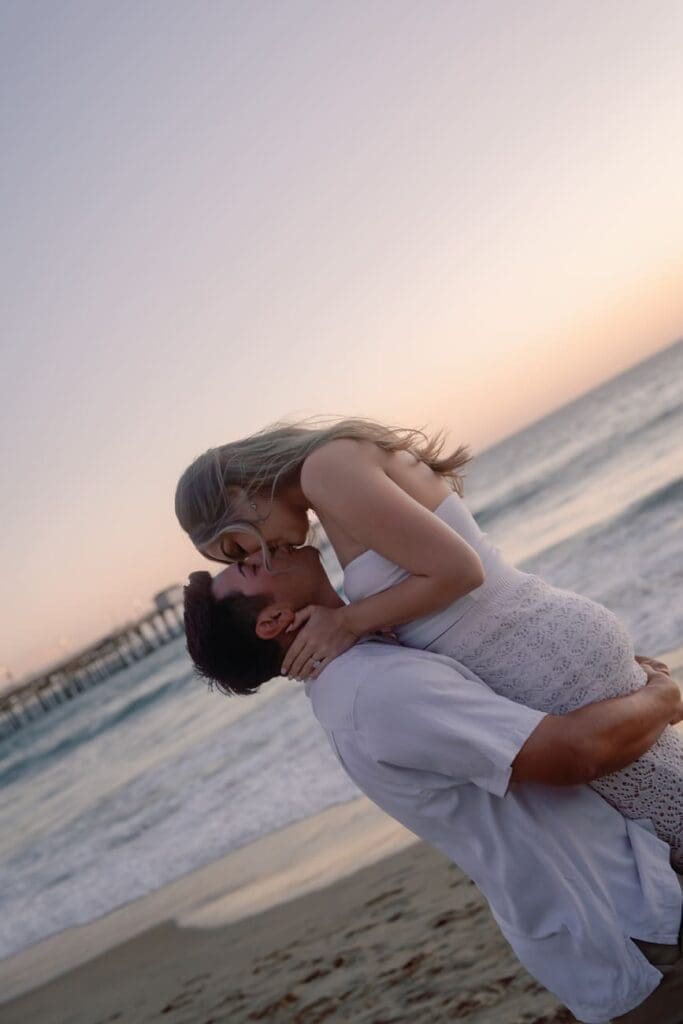 Couple laughing during a playful lift on San Clemente Beach after their Casa Romantica engagement session.