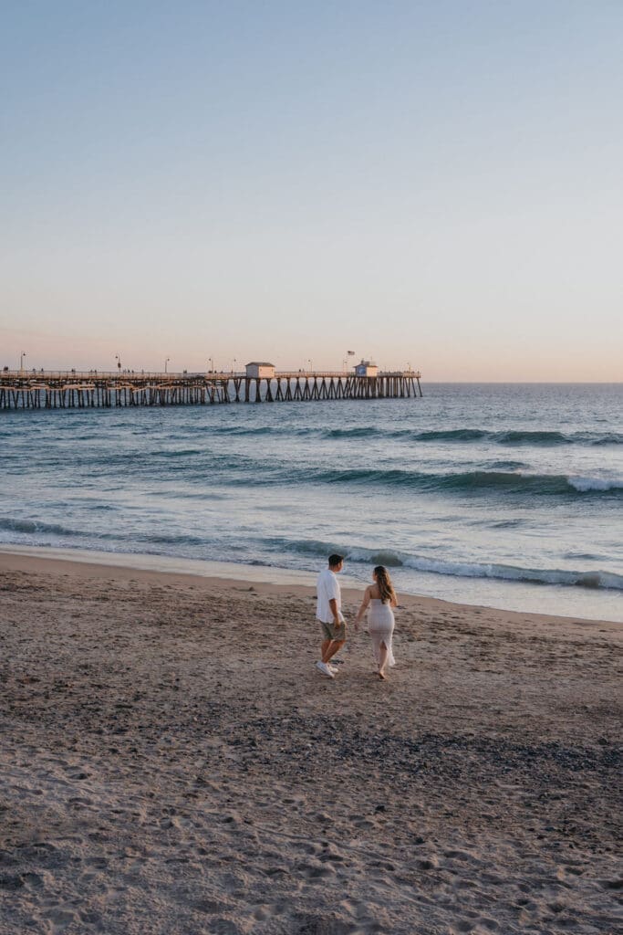 Wide beach photo of a couple near the San Clemente Pier during their coastal engagement session in Orange County.