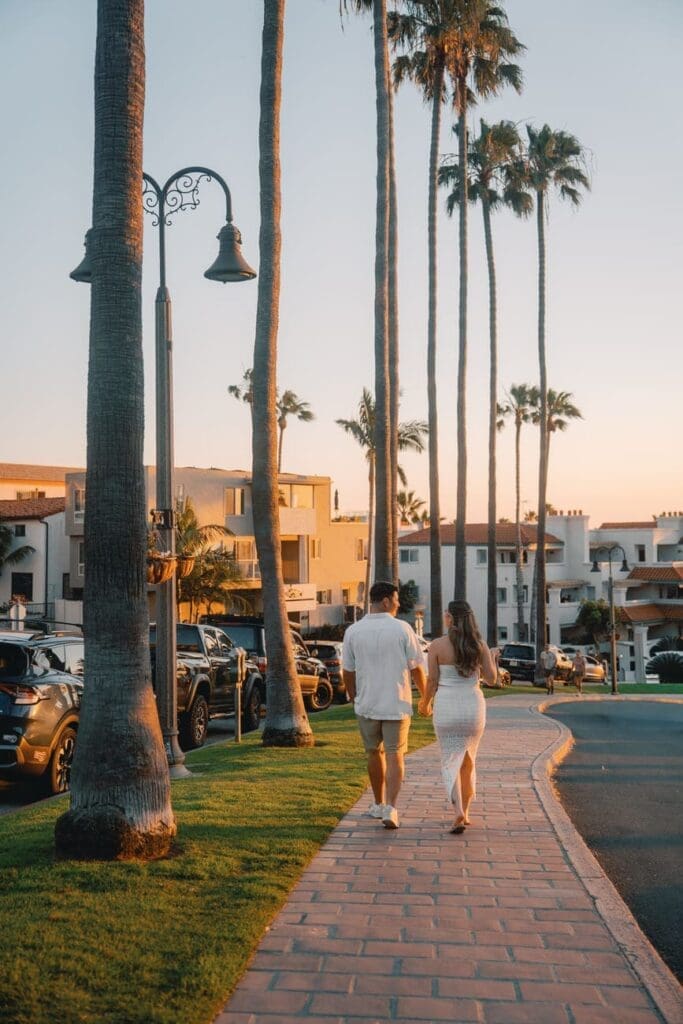 Couple walking from Casa Romantica toward San Clemente Beach for coastal engagement photos.
