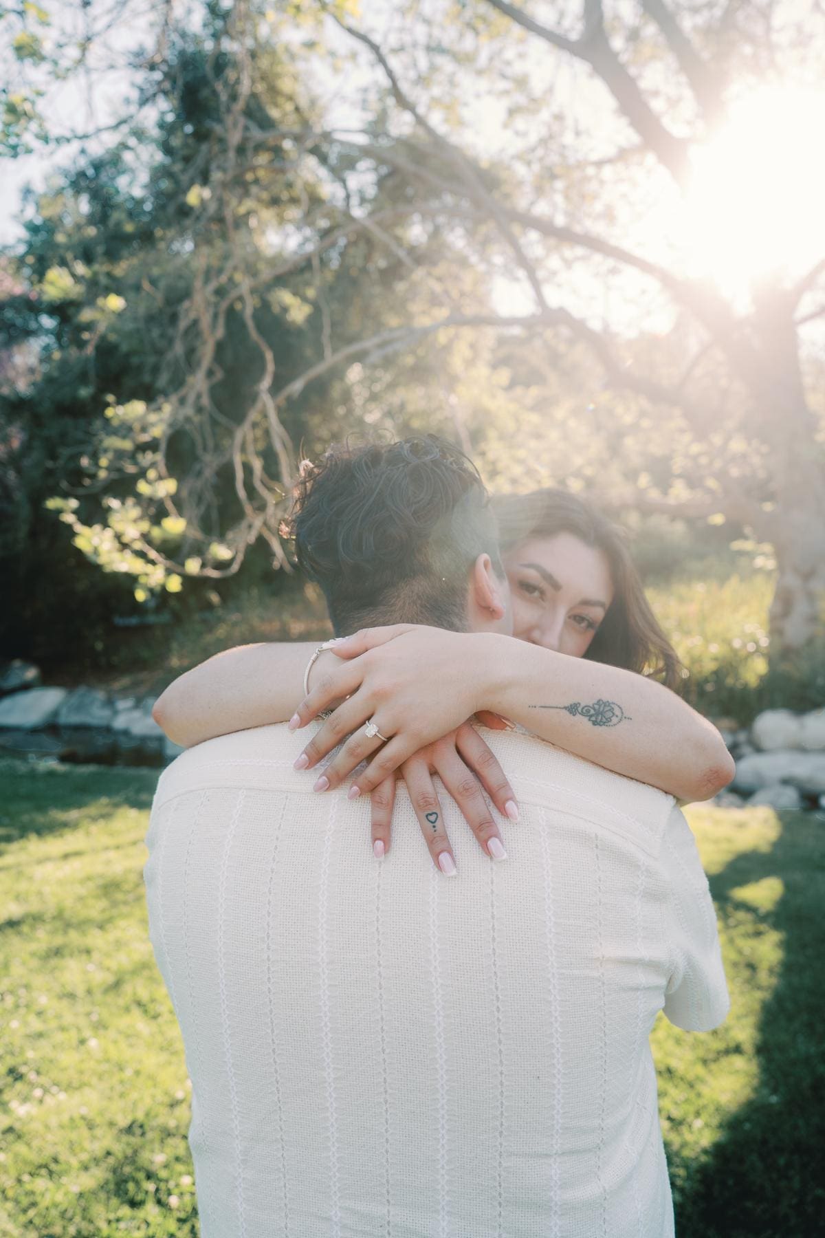 Woman embracing her partner with her engagement ring visible in warm backlight.