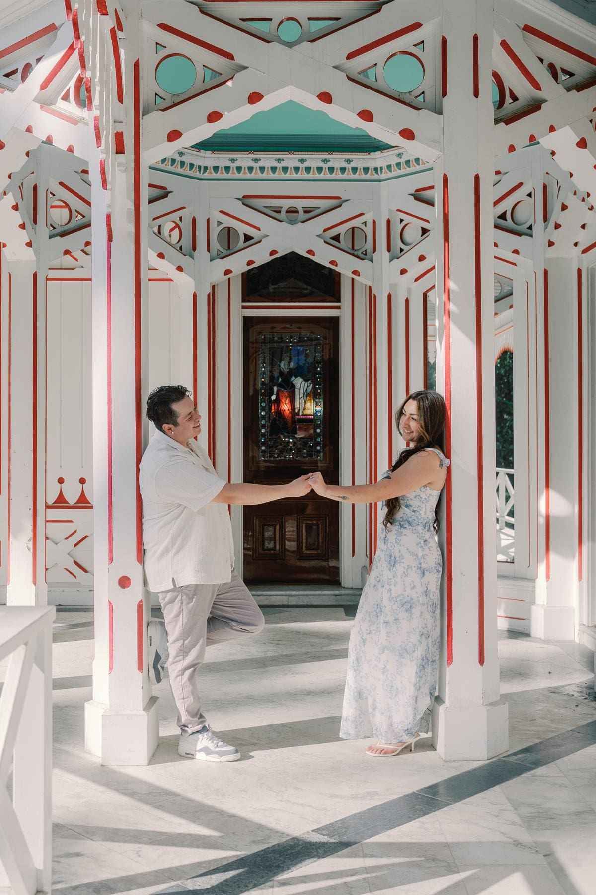 Couple holding hands beneath the ornate geometric details of a historic veranda.