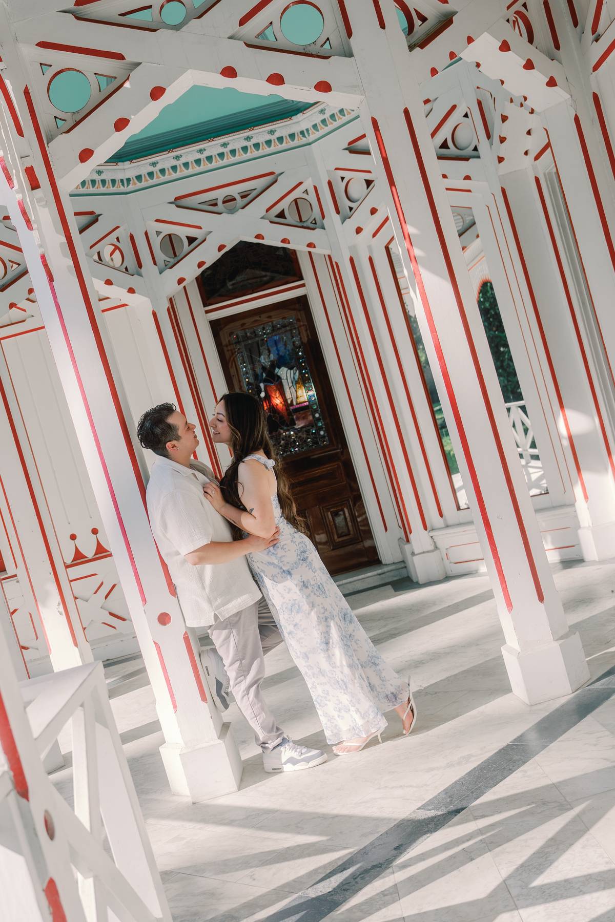 Couple kissing beneath the red and white framework of a historic veranda.