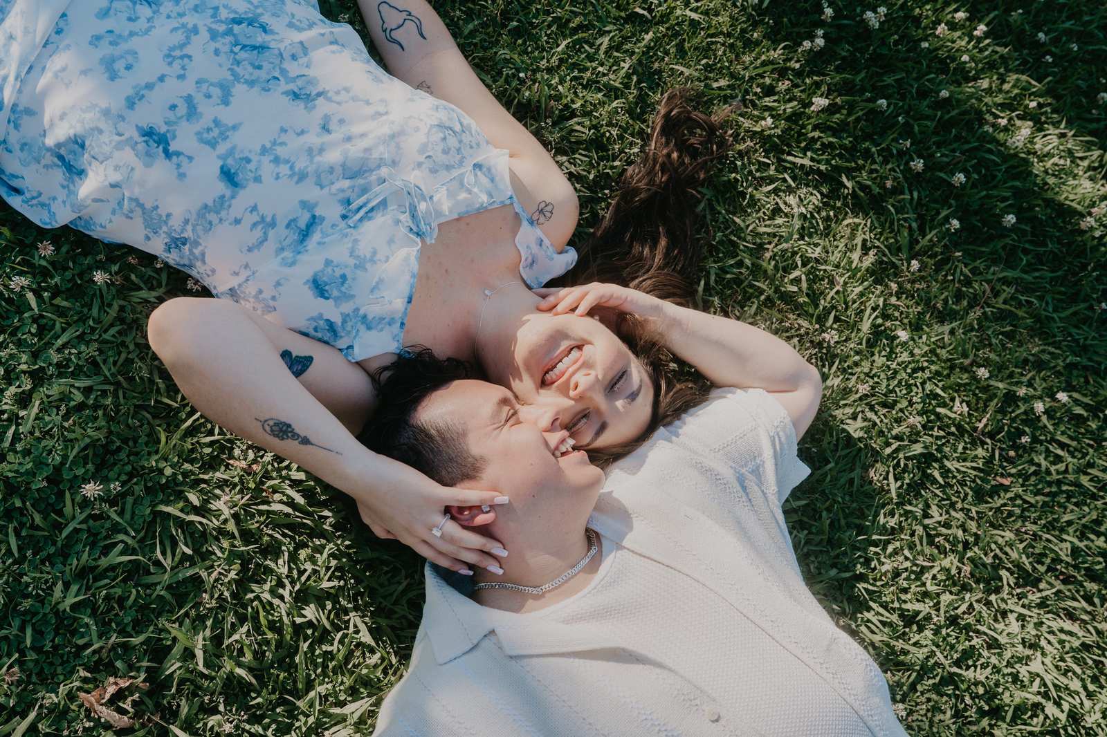 Overhead photograph of a couple lying together and laughing on the grass.