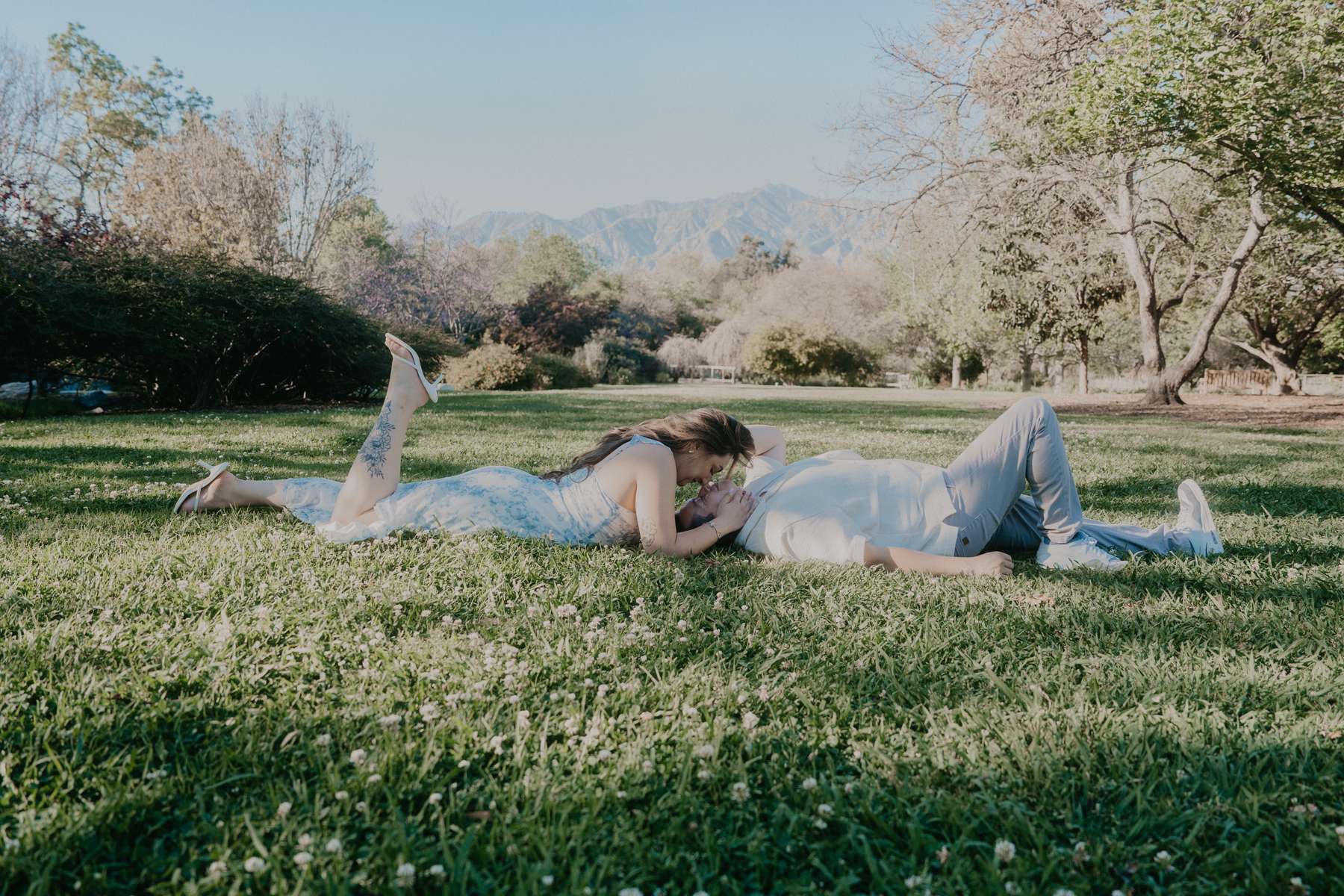 Couple lying together on a lawn with the San Gabriel Mountains in the distance at the LA Arboretum.