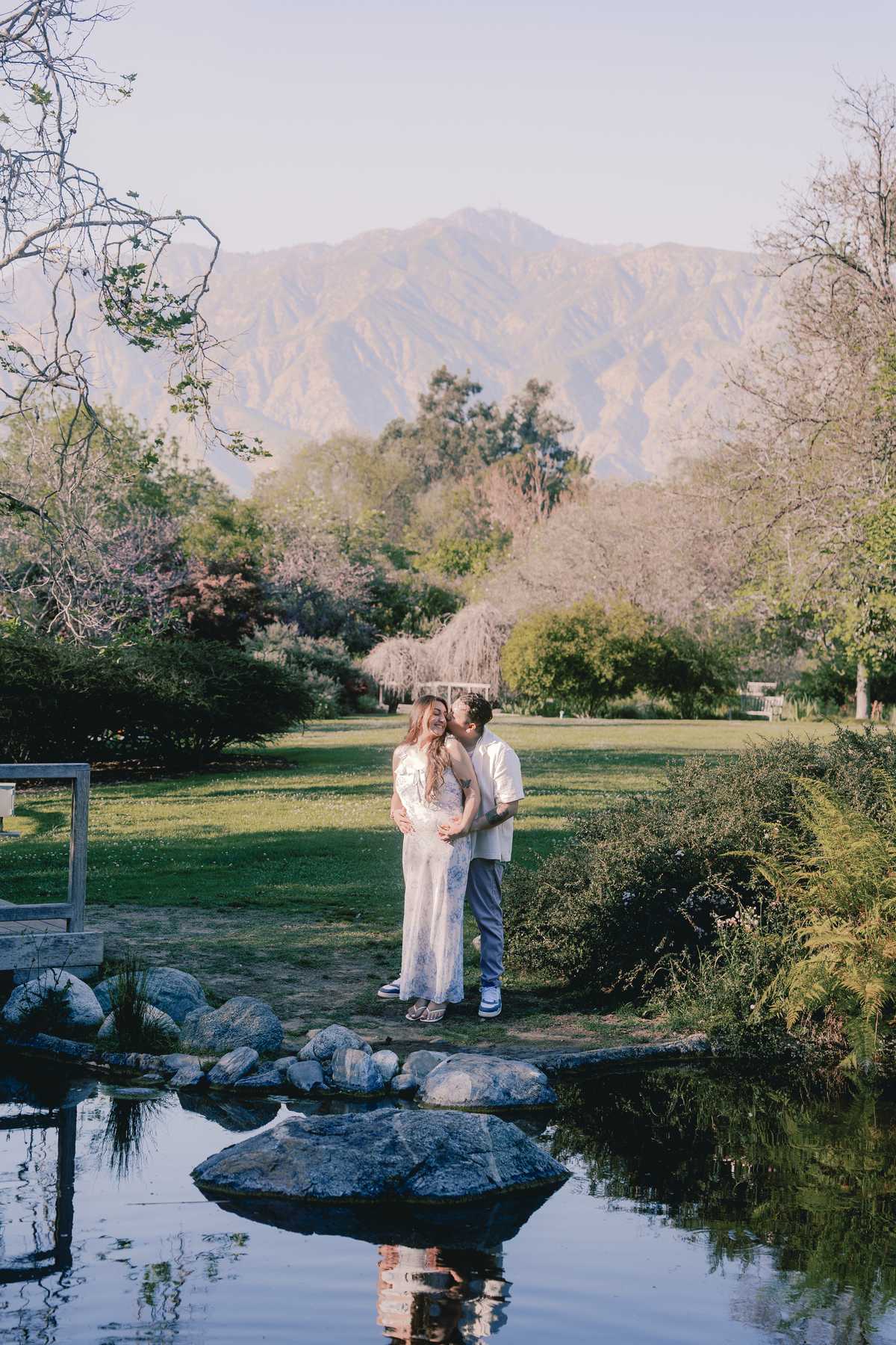 Couple standing beside a pond with the San Gabriel Mountains in the background.