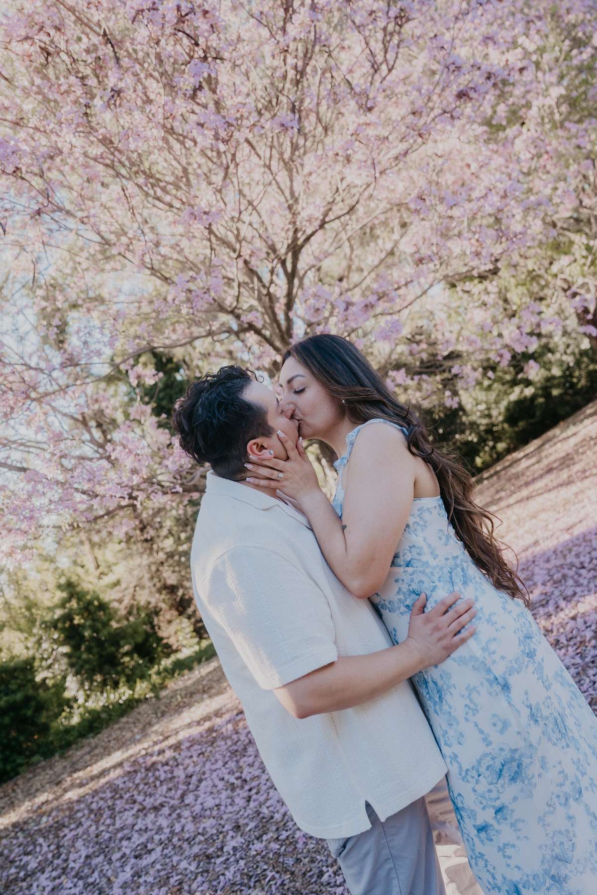 Couple kissing beneath a blooming pink tree during their spring engagement session.