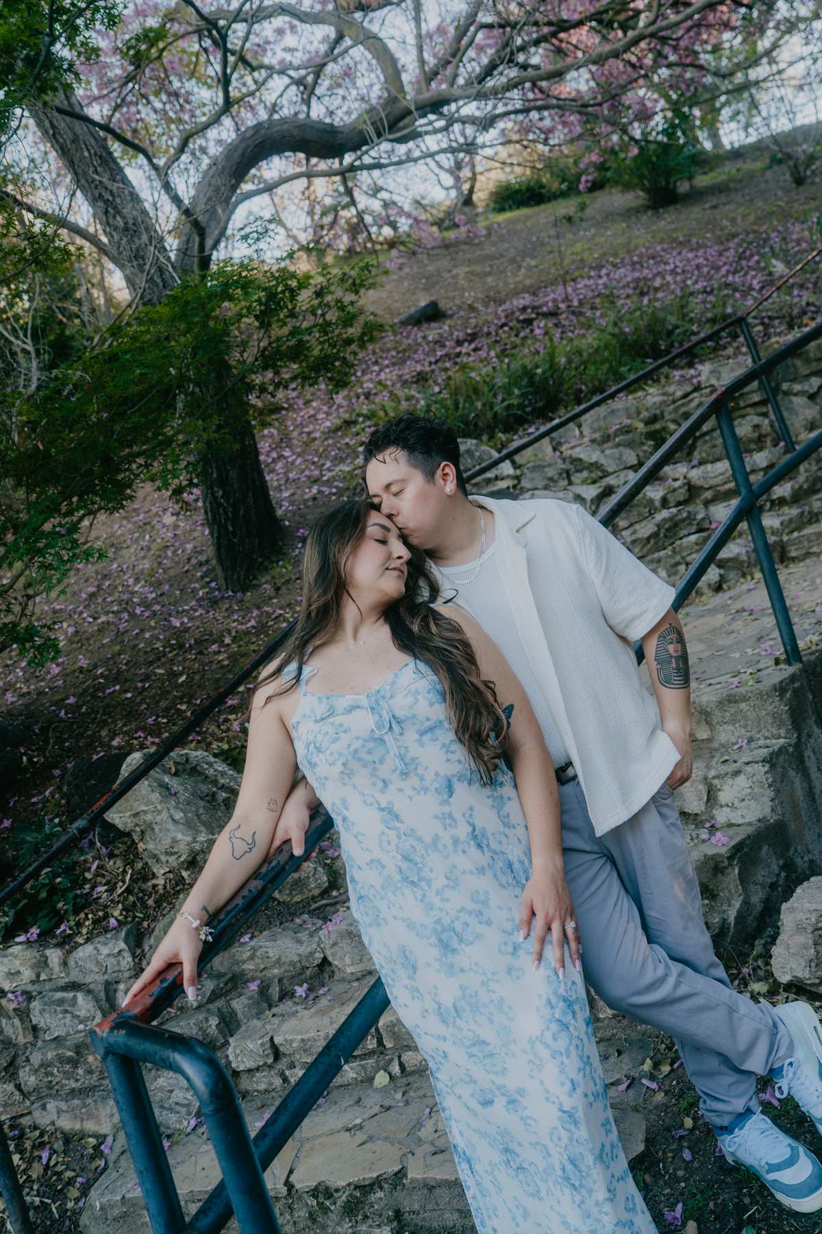 Couple standing together on stone steps beneath a tree covered in pink blossoms.