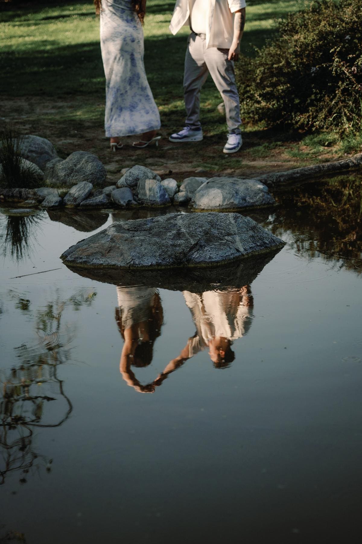 Couple making a heart with their hands in a quiet pond reflection.