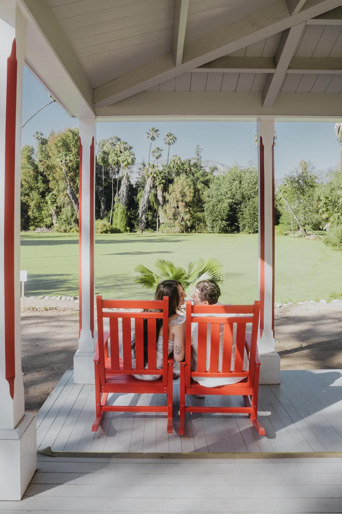 Couple sitting in red chairs on a shaded porch overlooking the garden.