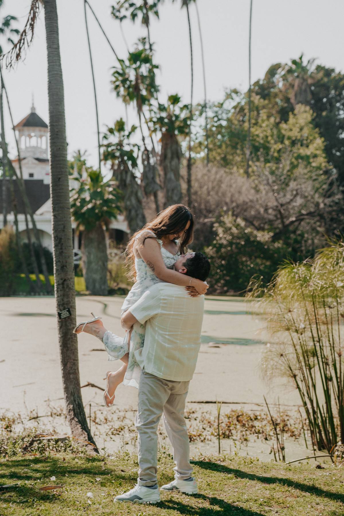 Couple embracing on the lawn near Queen Anne Cottage at the LA Arboretum.
