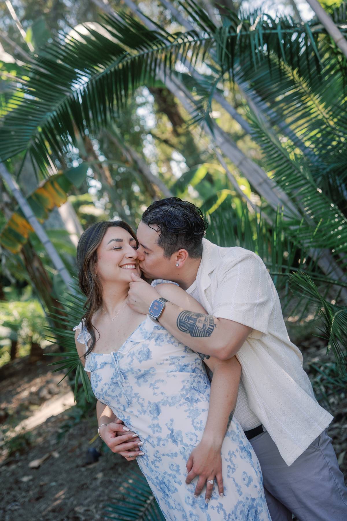 Man kissing his partner's cheek among tropical palms at the LA Arboretum.