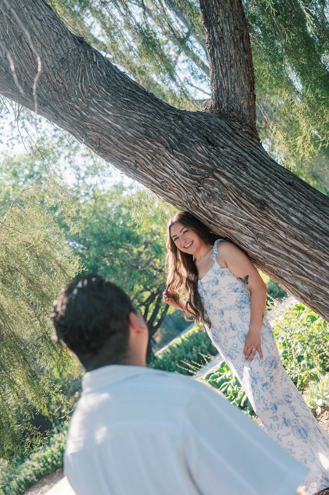 Woman laughing with her partner beneath the curved trunk of a willow tree.