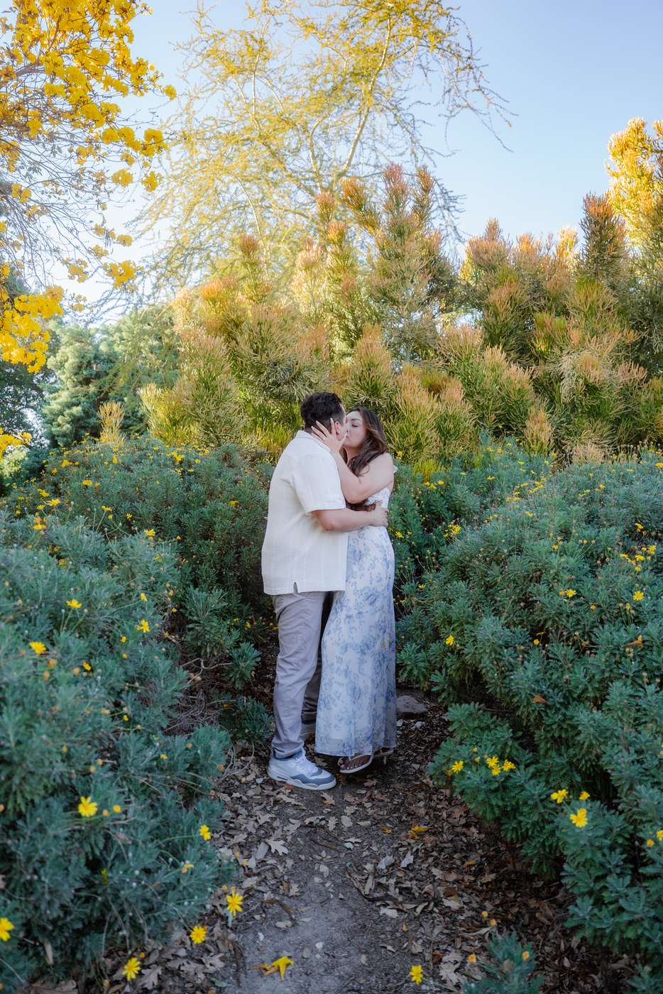 Couple embracing along a narrow path surrounded by yellow wildflowers.