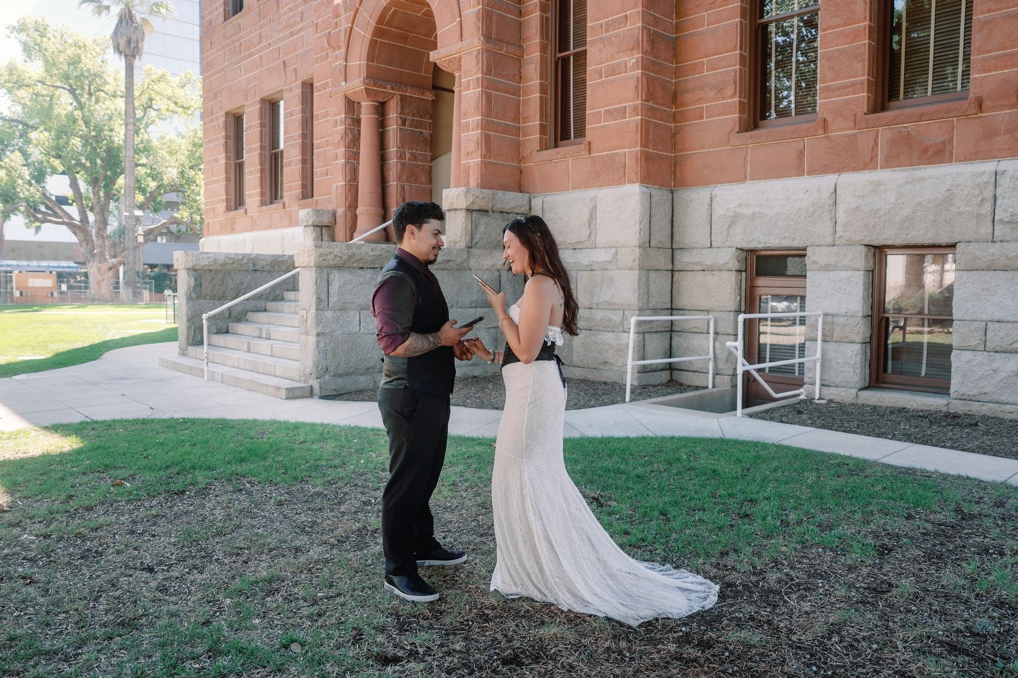 The couple faces each other on shaded grass beside the Old Orange County Courthouse in Santa Ana, California.