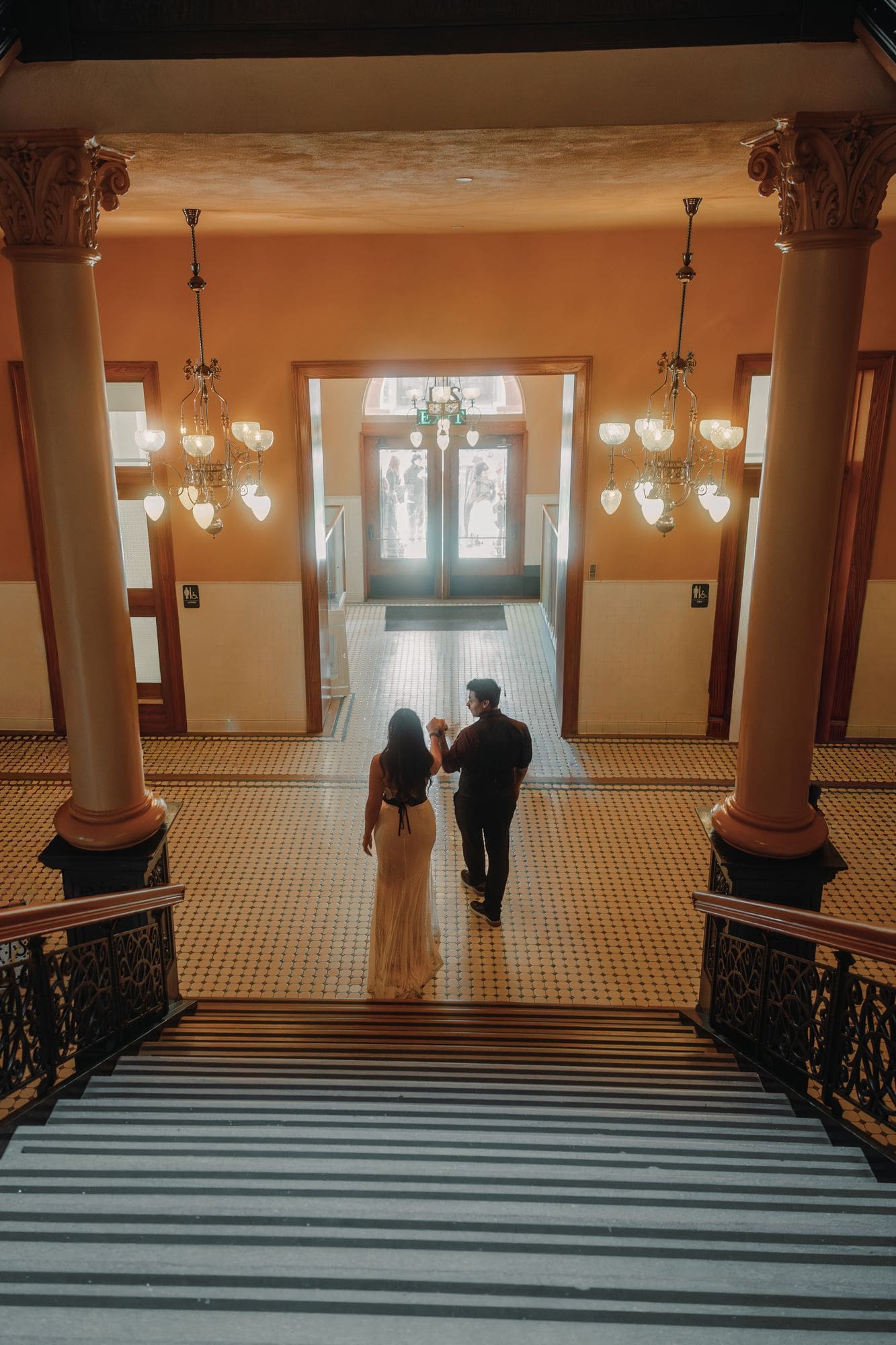 The couple descends the grand staircase beneath chandeliers at the Old Orange County Courthouse in Santa Ana.