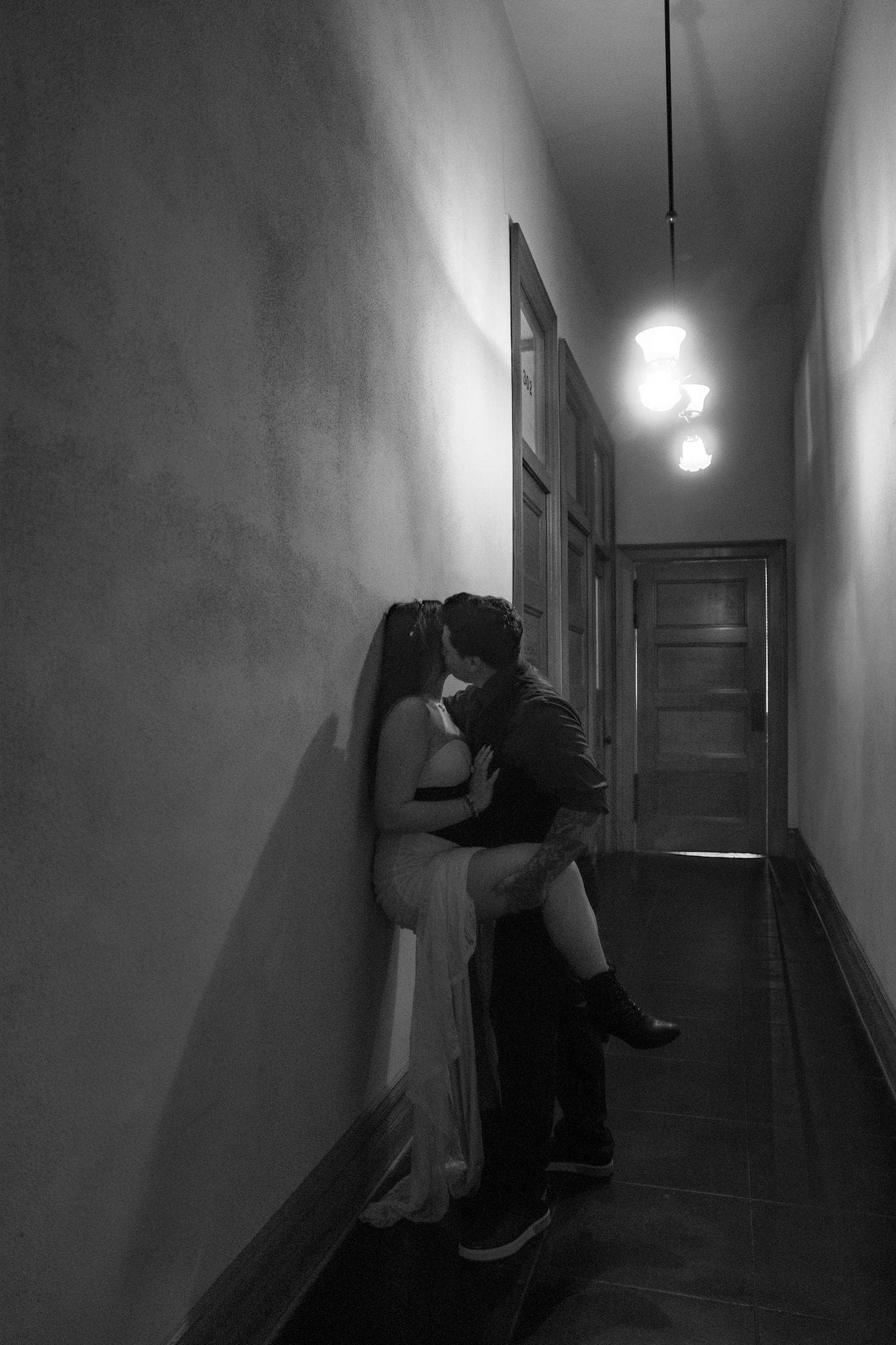A black-and-white portrait of the couple kissing in a narrow hallway.