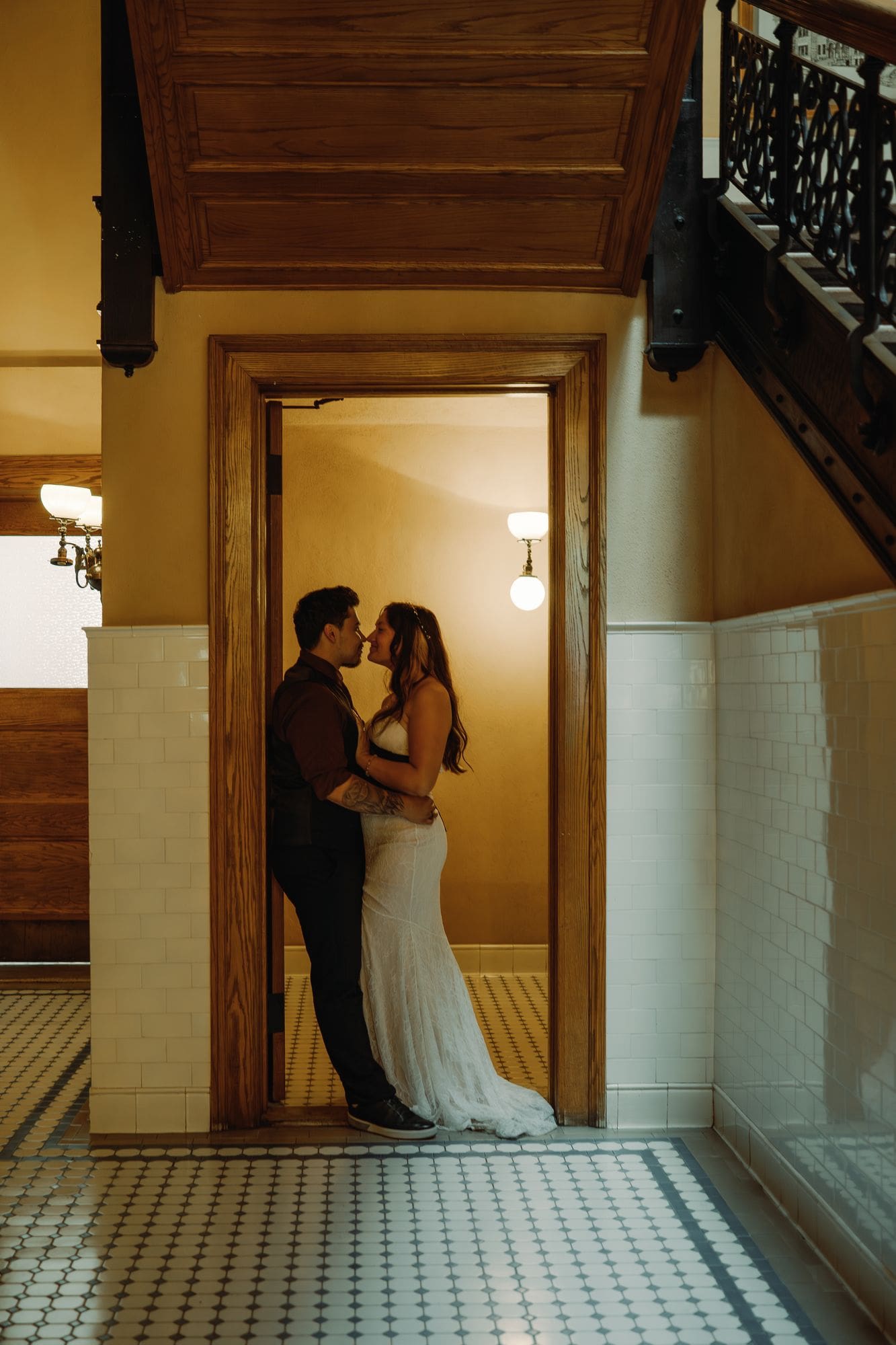The couple kisses in a wooden doorway below the interior staircase.