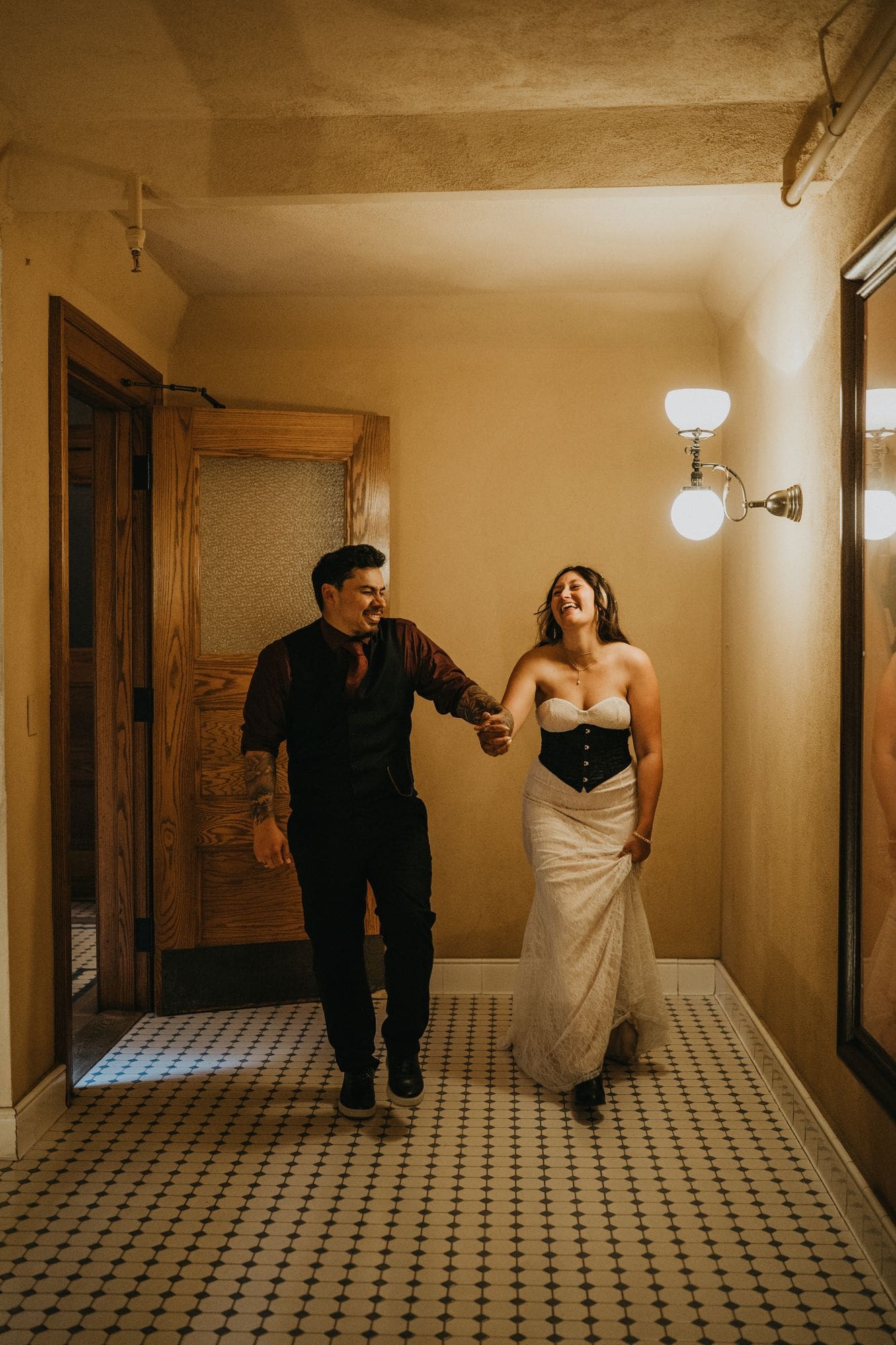 The couple laughs while walking hand in hand along a tiled courthouse hallway.