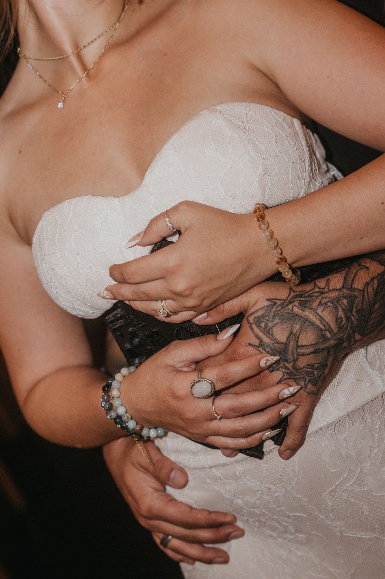 The couple’s hands overlap at the waist of a white lace dress, with their rings visible.