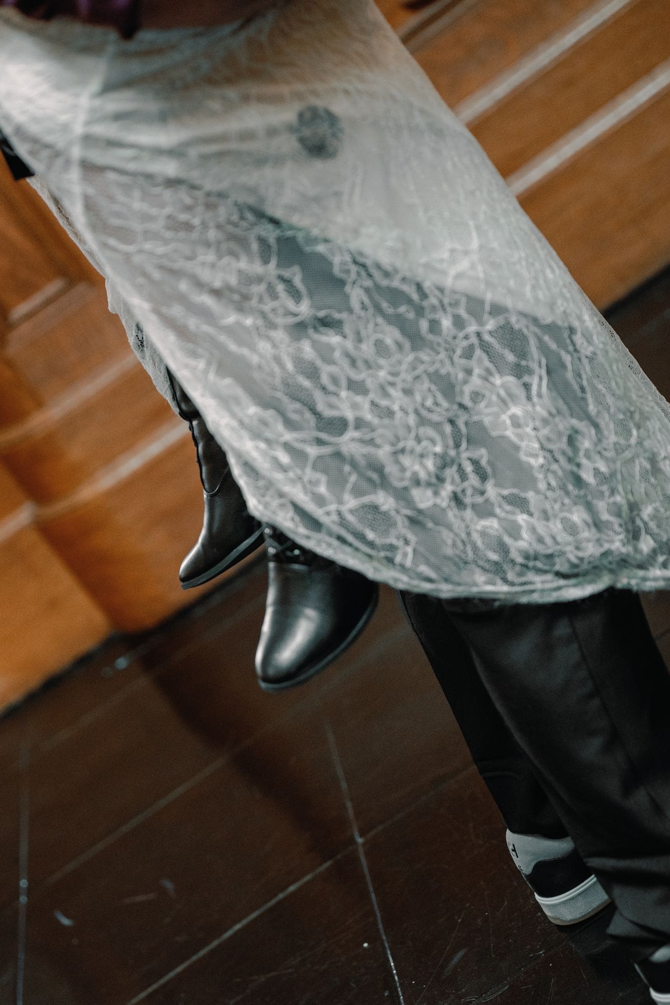 White lace and black boots beside the groom’s trousers during indoor portraits.