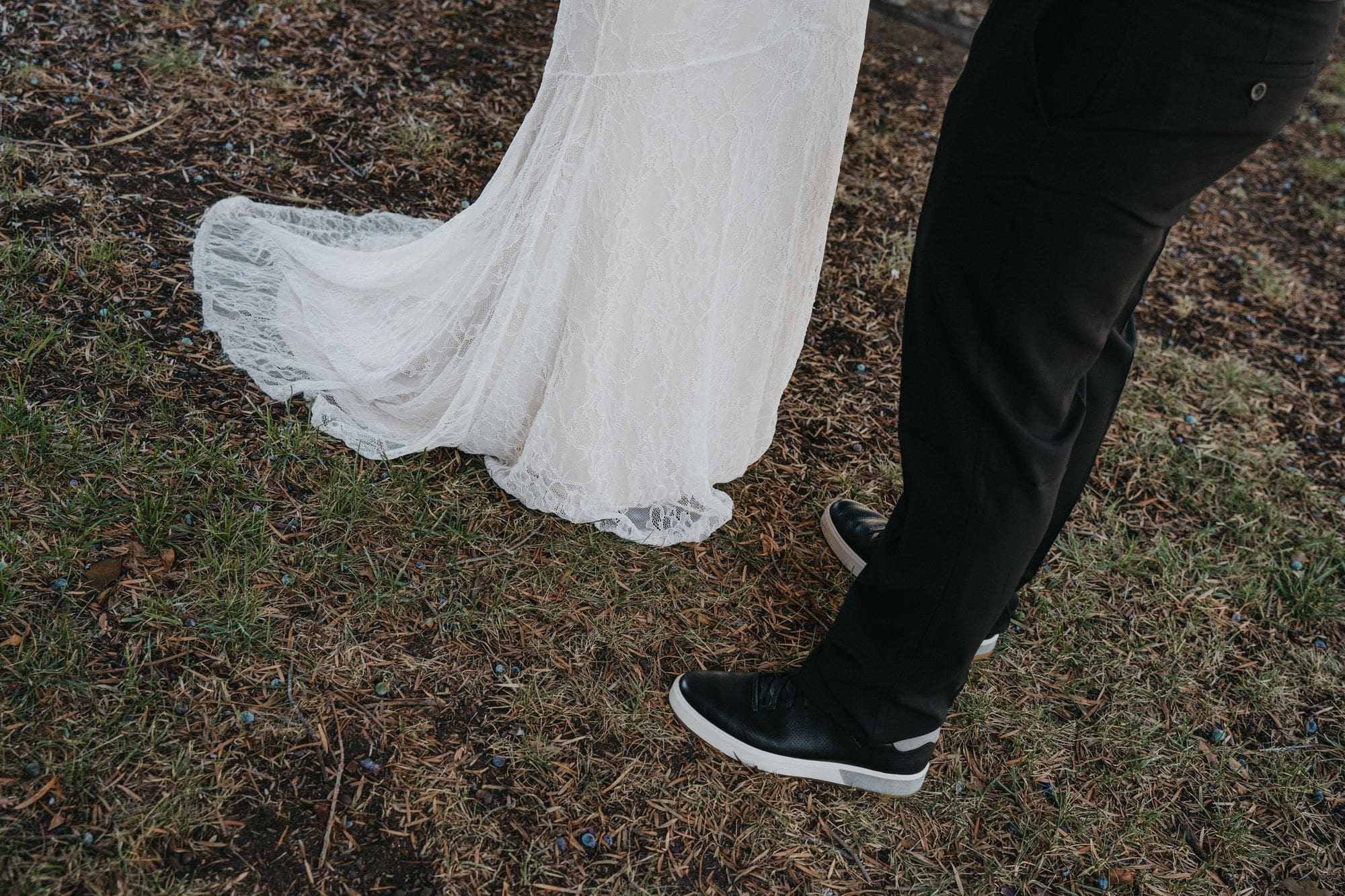 The couple’s black shoes and the hem of a white lace dress on the grass.