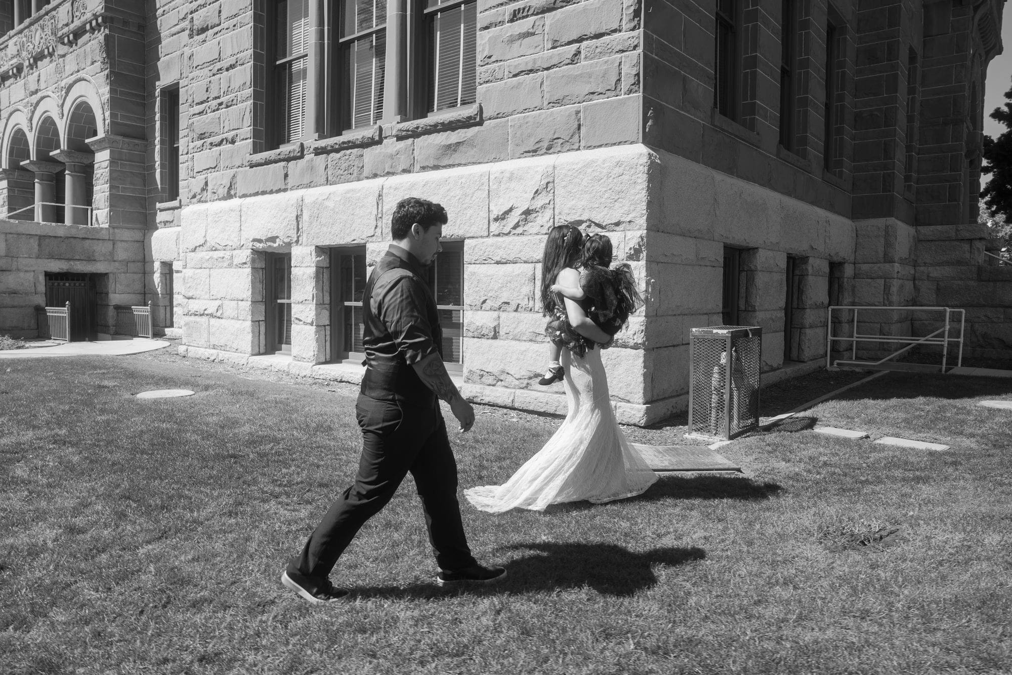 A black-and-white photograph of the couple walking together beside the courthouse stone walls.