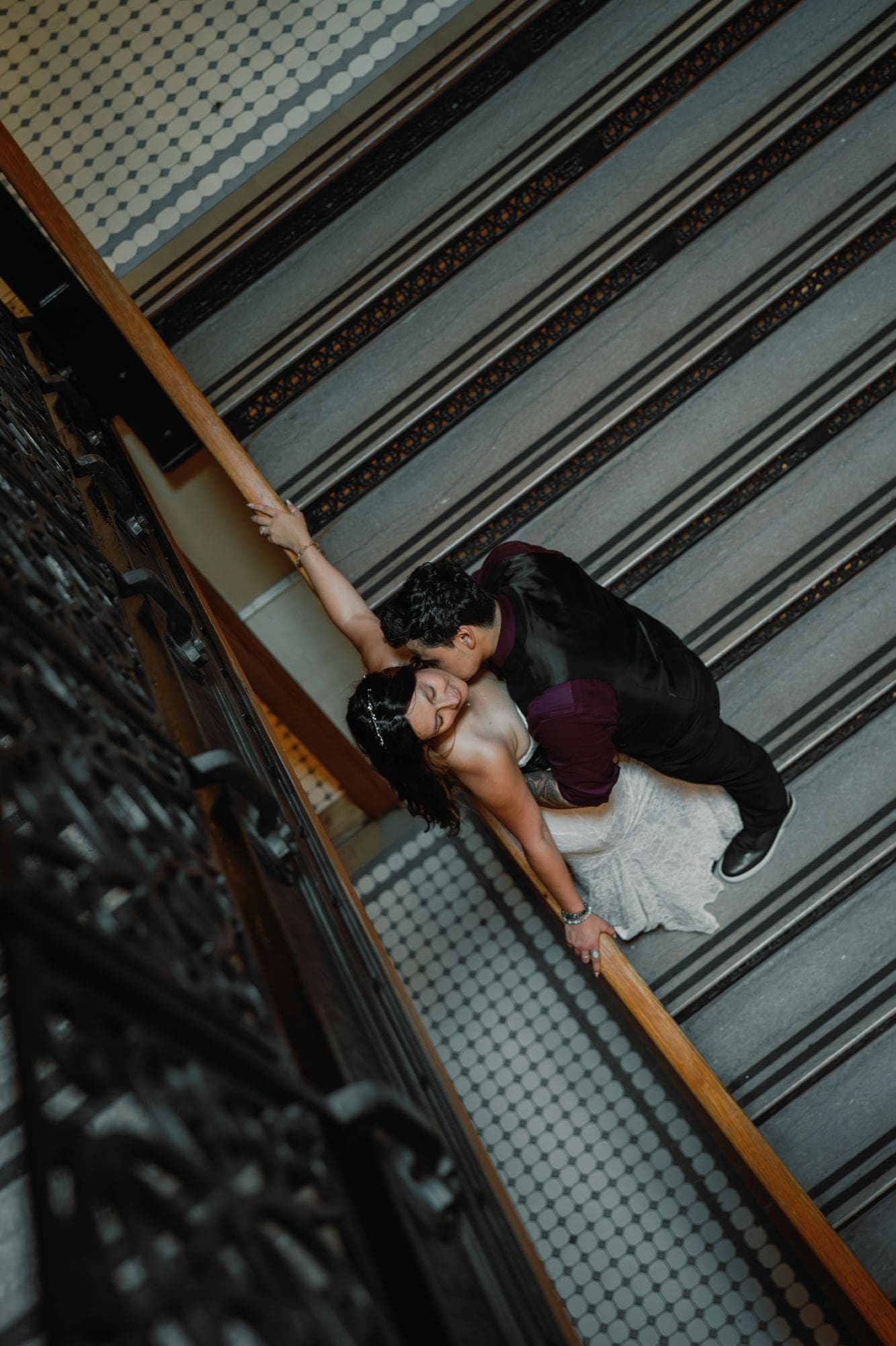 An overhead view of the couple embracing on the courthouse staircase, with the bride holding a wooden handrail.