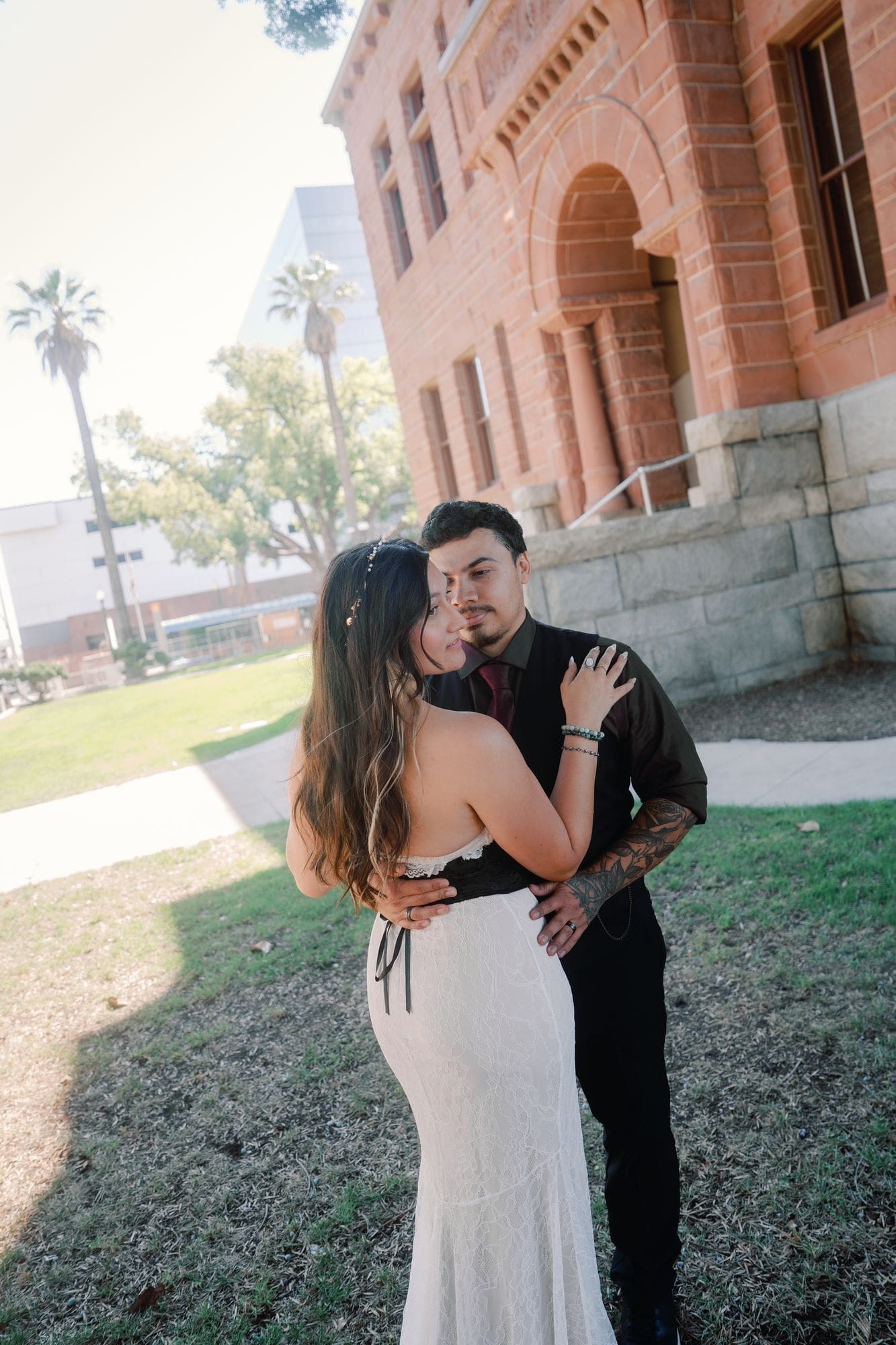 The couple embraces in the shade beside the courthouse’s red stone arch.