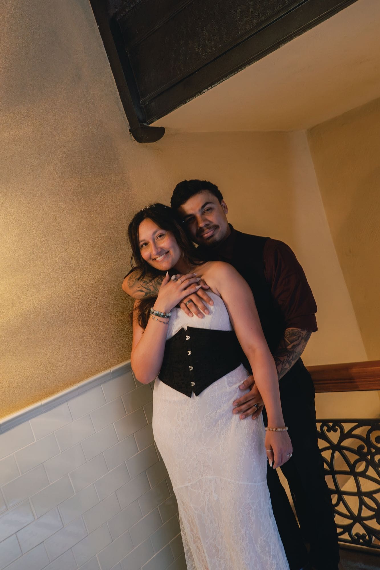 The couple shares a close embrace against a warm-toned staircase wall.