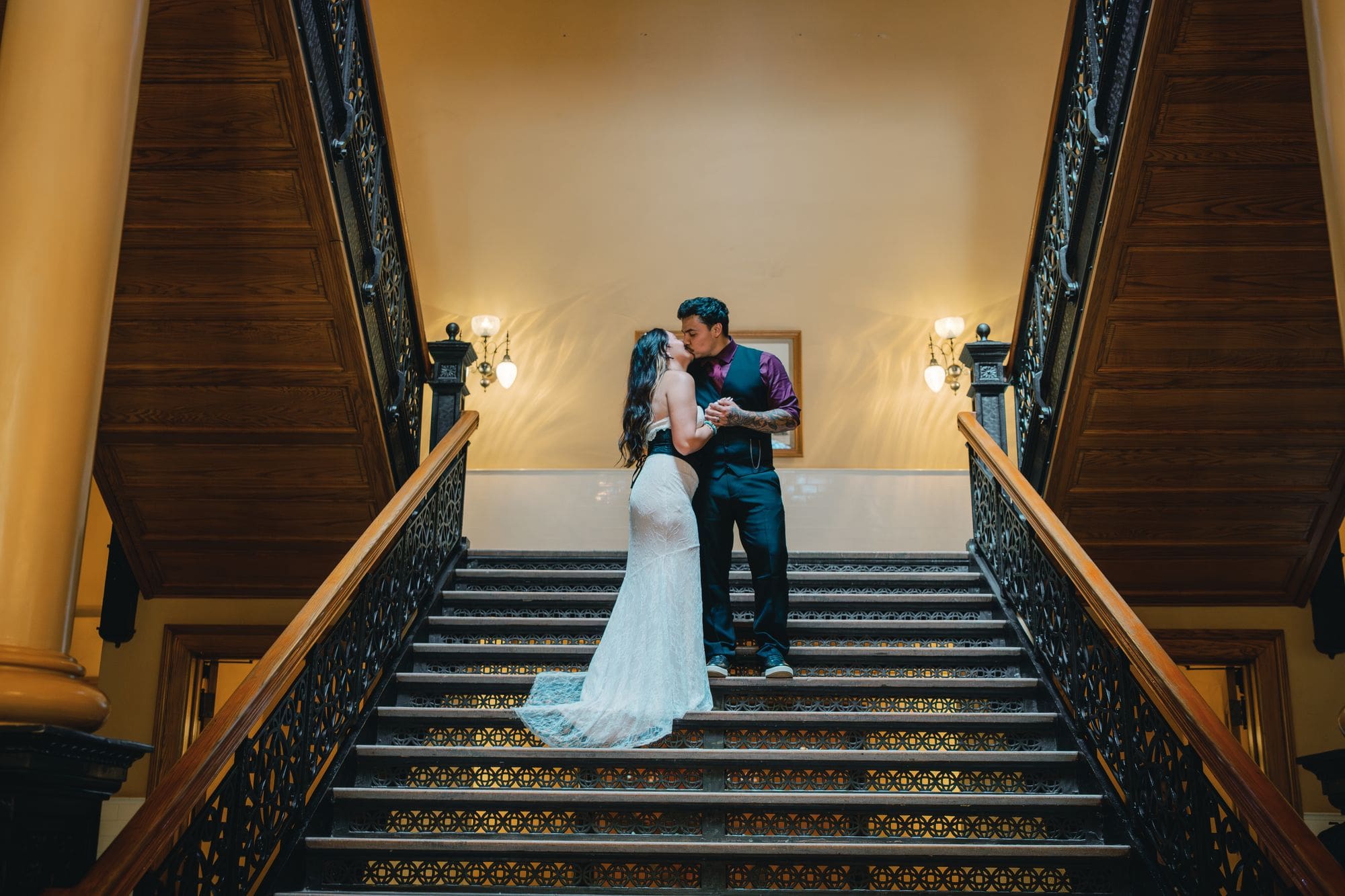 A couple kisses on the wooden staircase during Santa Ana courthouse wedding portraits at the Old Orange County Courthouse.