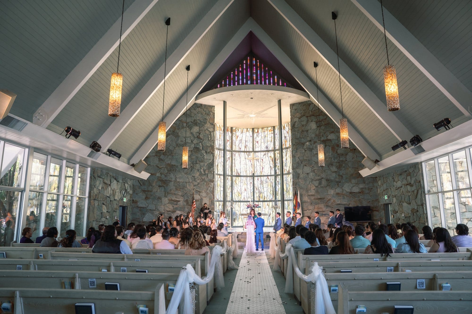 Guests sit beneath the peaked sanctuary ceiling as the couple stands at the front during a Santa Anita Church wedding in Arcadia, California.