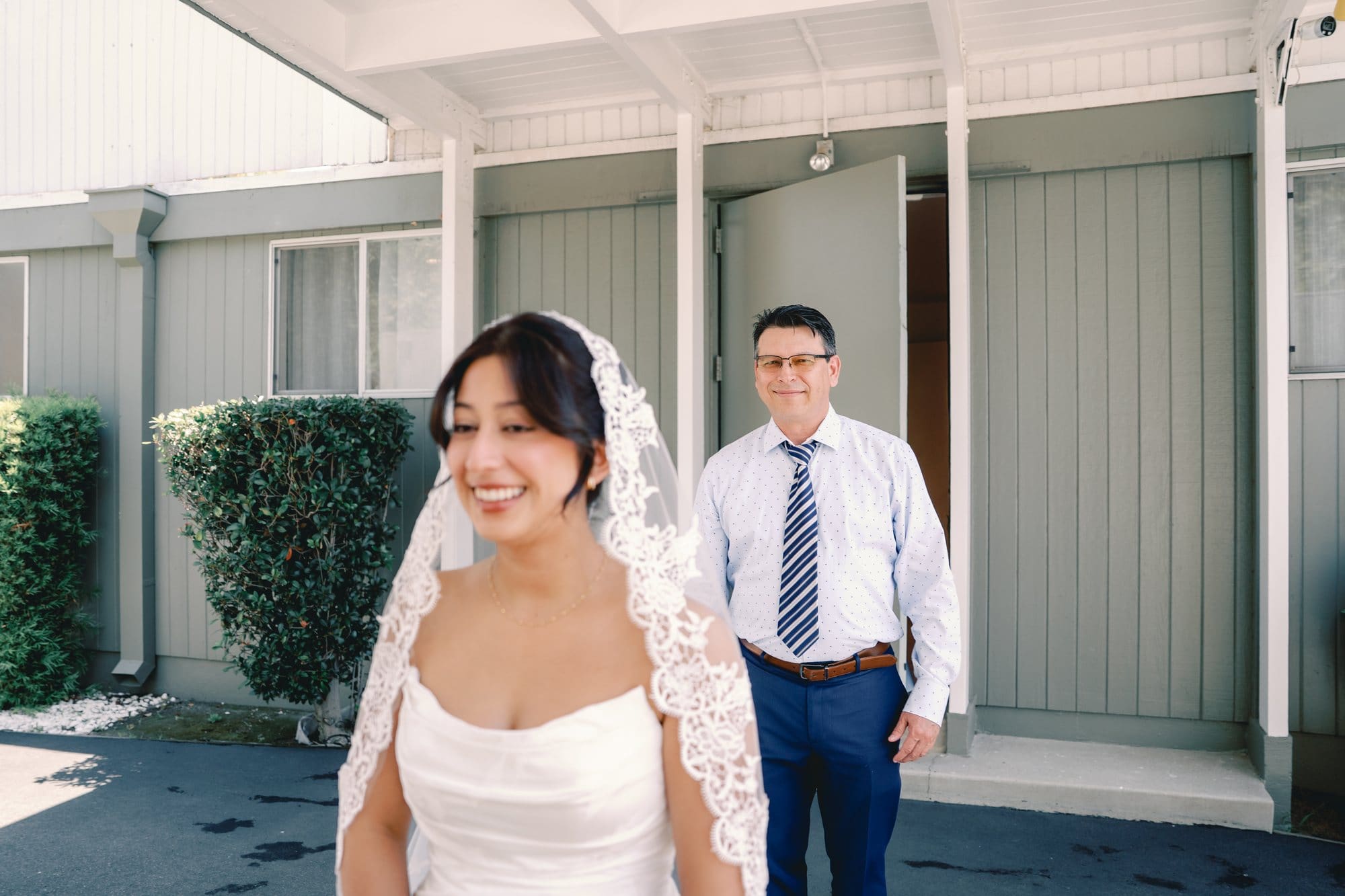 The bride smiles as her dad approaches from behind outside the bridal suite at The Santa Anita Church in Arcadia, California.