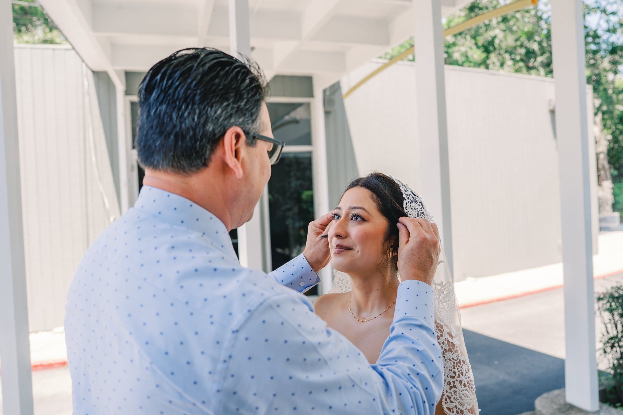The bride looks up at her dad as he holds her during their first look at The Santa Anita Church in Arcadia, California.