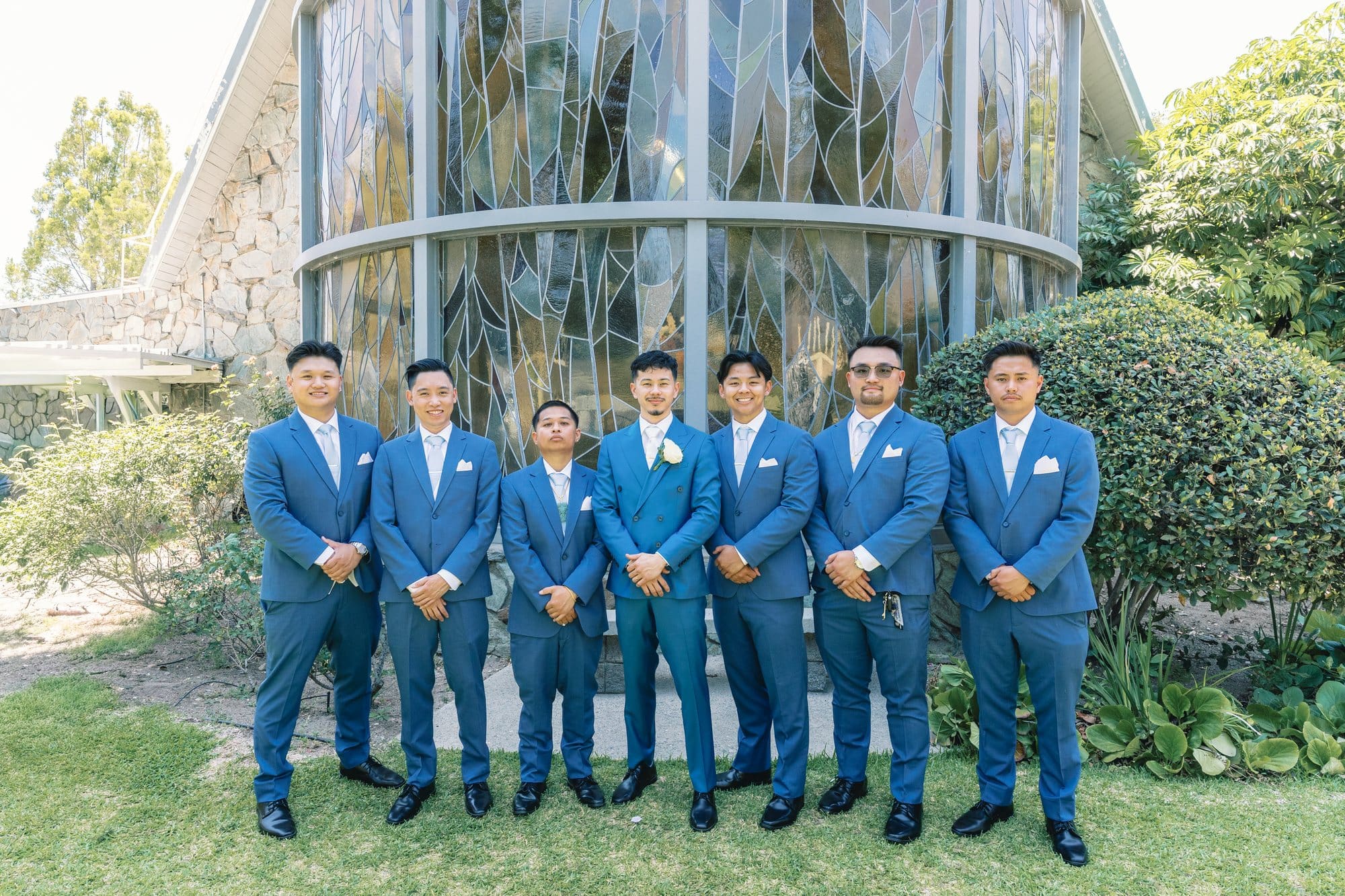 The groom stands with groomsmen in blue suits on the lawn at The Santa Anita Church in Arcadia, California.