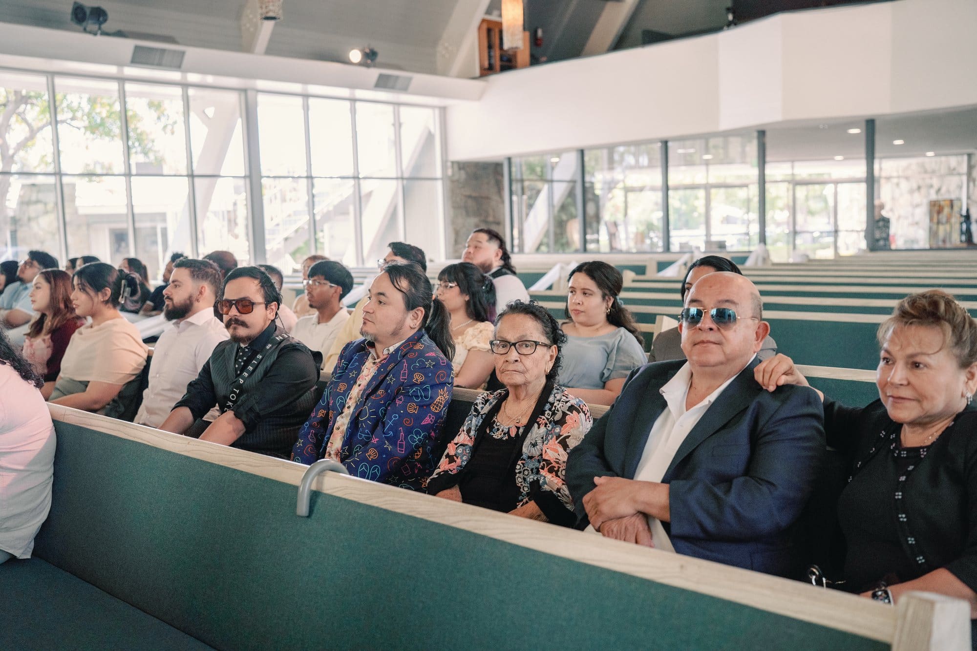 Wedding guests watch from rows of teal sanctuary pews at The Santa Anita Church in Arcadia, California.
