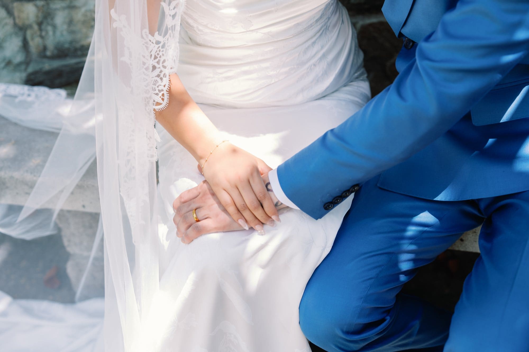 A close view shows the couple’s joined hands resting on the wedding dress and blue suit at The Santa Anita Church in Arcadia, California.
