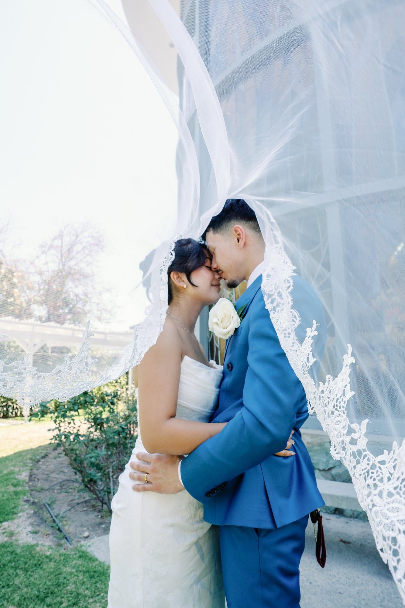 The couple kisses beneath the bride's lifted veil outdoors during a Santa Anita Church wedding in Arcadia, California.