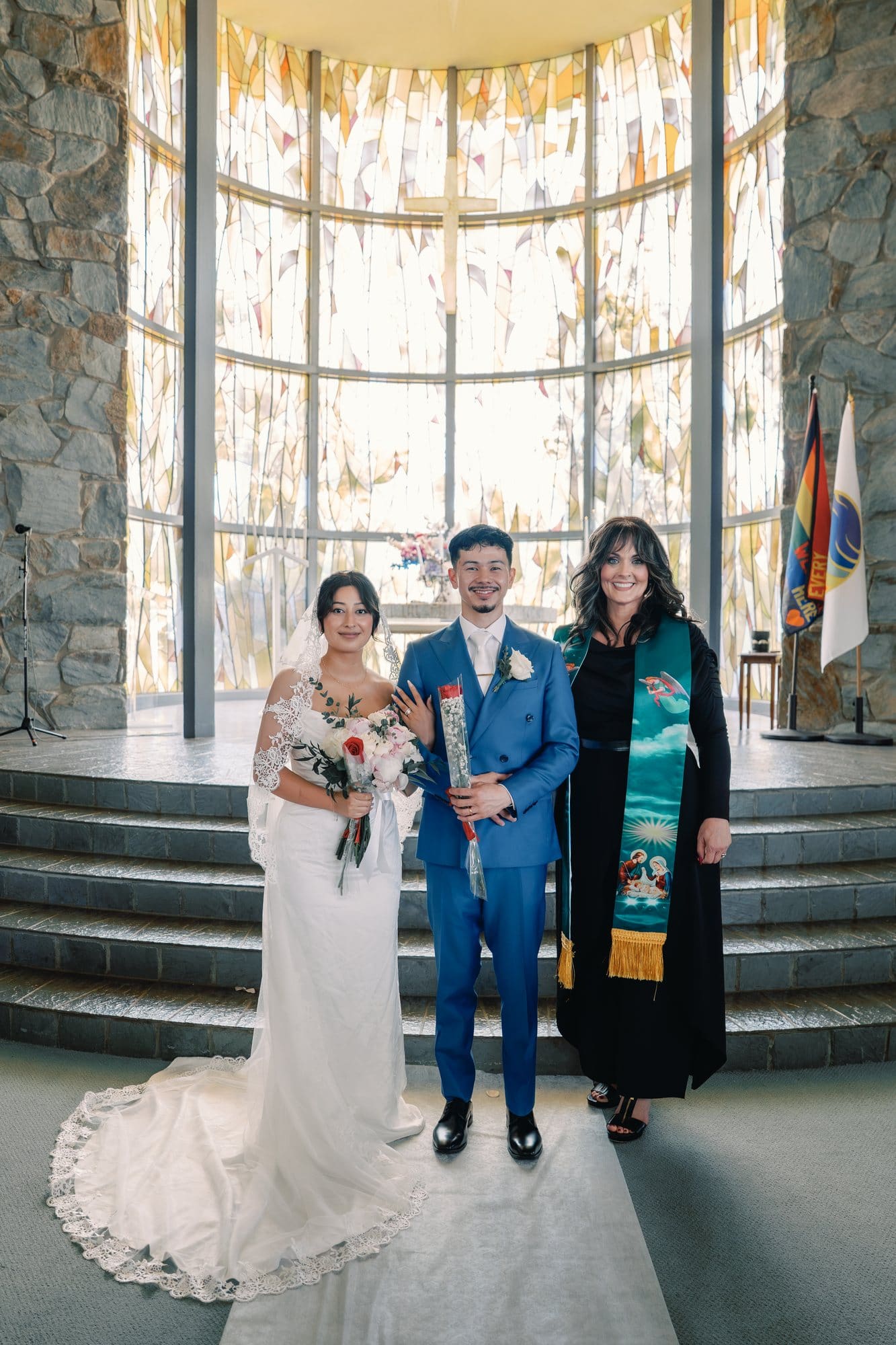 The couple poses with the officiant beside the sanctuary steps at The Santa Anita Church in Arcadia, California.