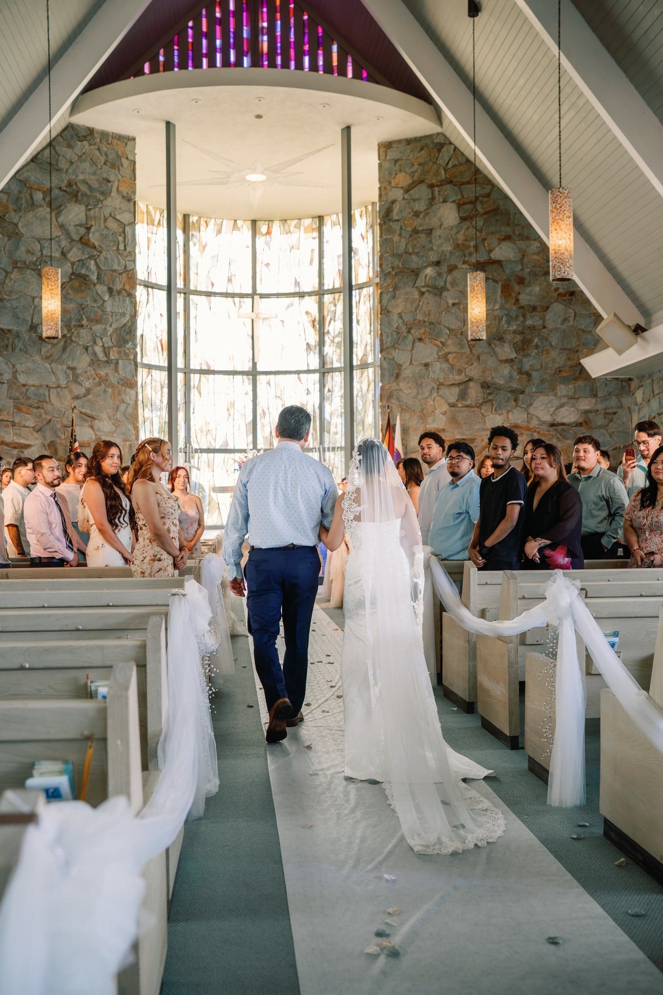 The bride and her dad walk down the aisle toward the stained glass at The Santa Anita Church in Arcadia, California.