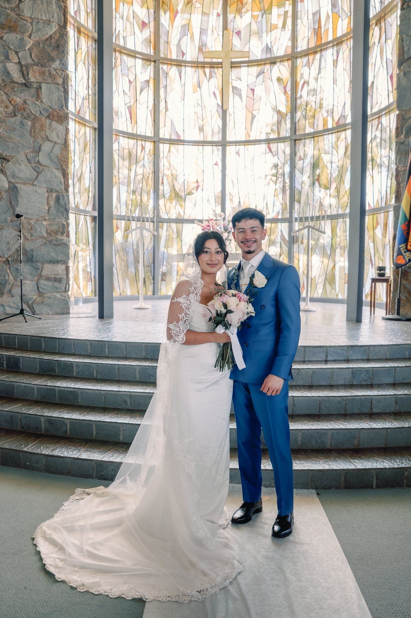 The couple stands together in front of the Tower of Light with the bride's train spread out during a Santa Anita Church wedding in Arcadia, California.